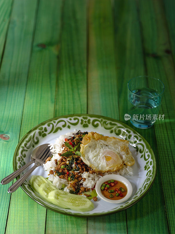著名的泰国辣菜“Pak Krapao Moo”，英文是用圣罗勒炸猪肉，在一张古老的绿色风化木桌子上，用蒸饭、煎蛋、黄瓜和“Pik Nam Bla”(鱼酱辣椒)。